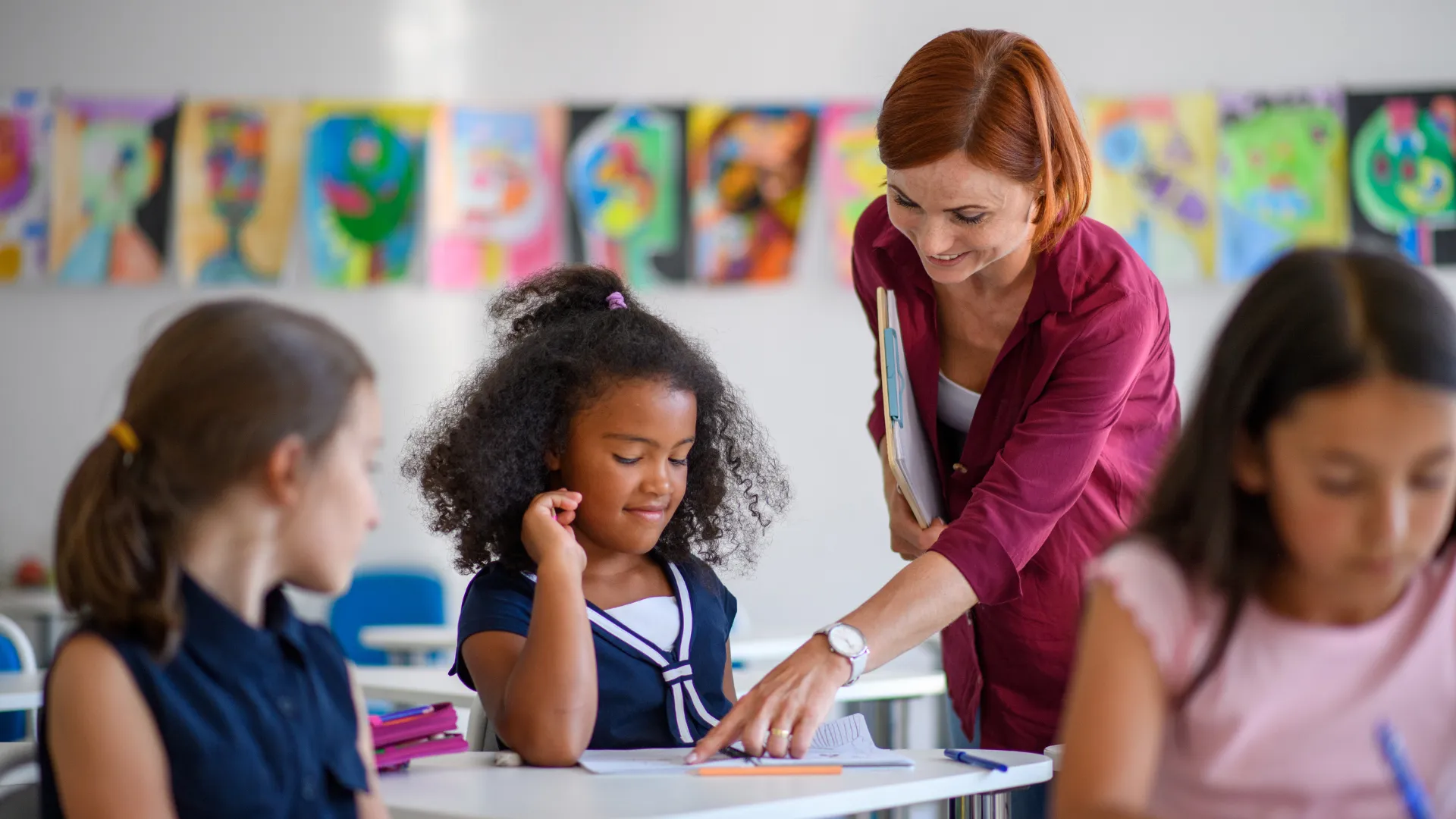 A teacher assisting students in a classroom with colourful artwork on the walls