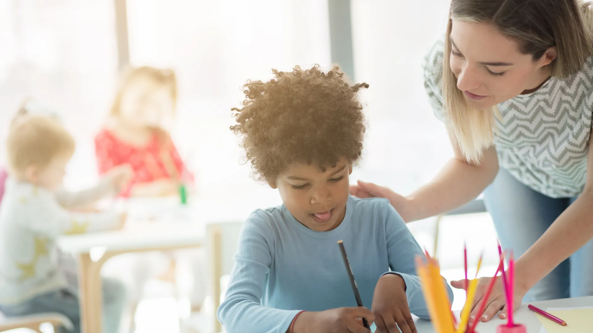Children in a classroom with a teacher assisting a child