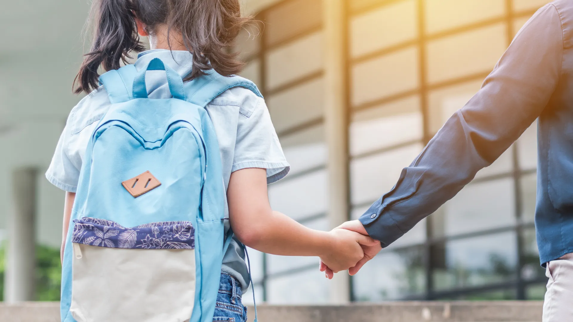Child with a backpack holding hands with an adult