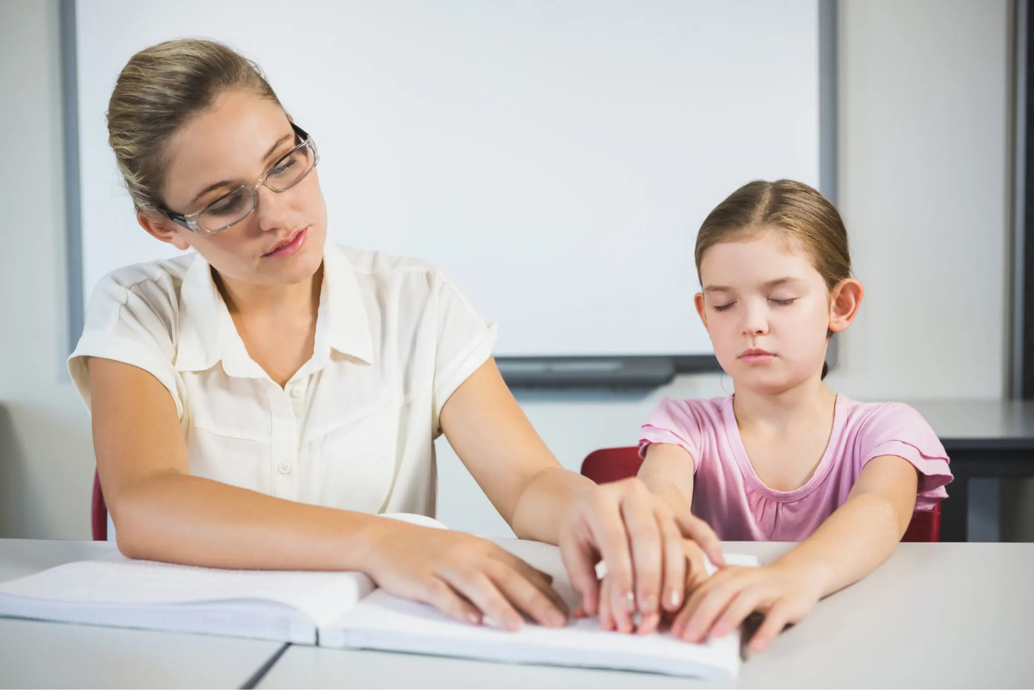A child reading Braille on a page, with an adult's hand guiding them