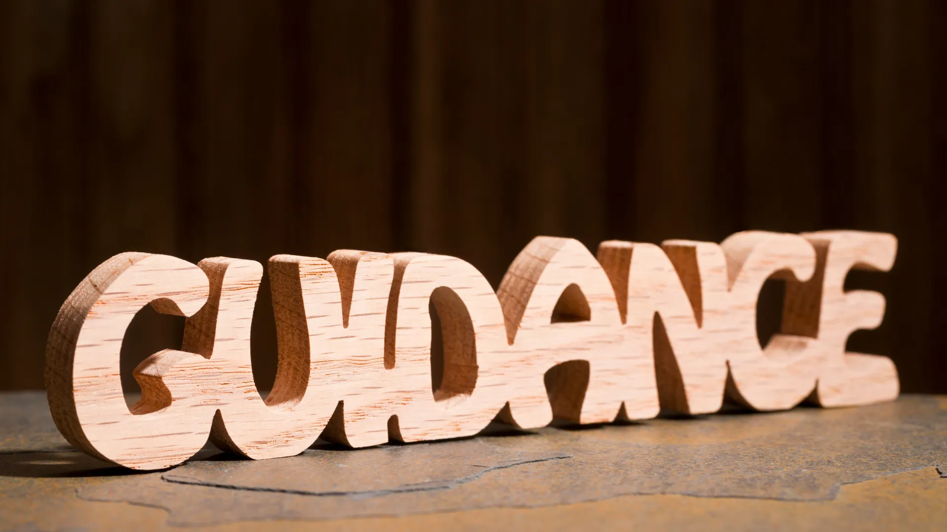 Wooden carving of the word 'GUIDANCE' placed on a surface with a dark background