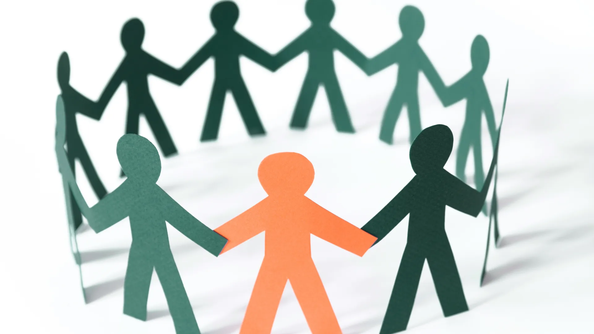 A group of paper persons holding hands in a circle, with one person in a different colour"
