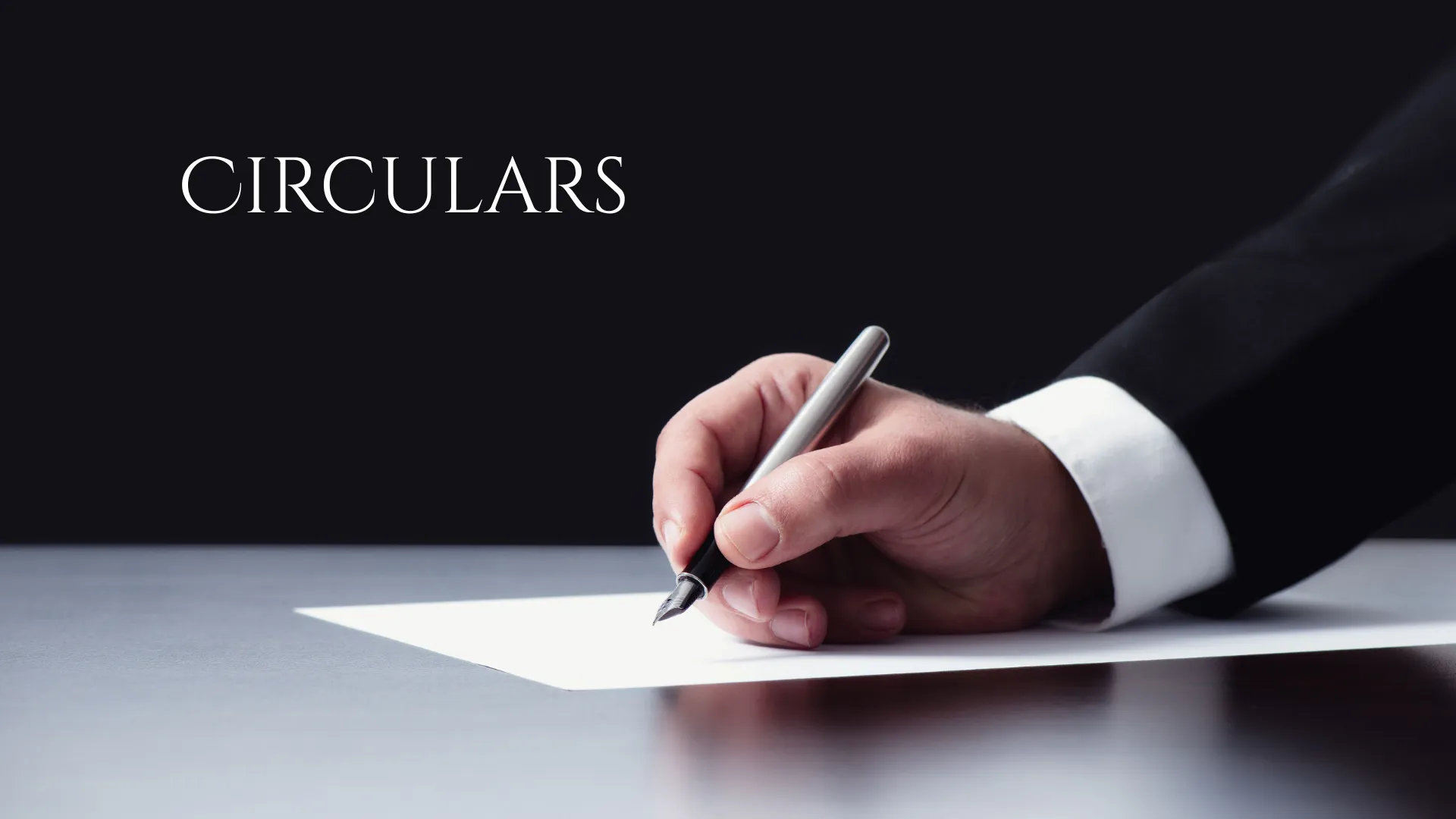 A person writing on a piece of paper with the word "CIRCULARS" displayed above