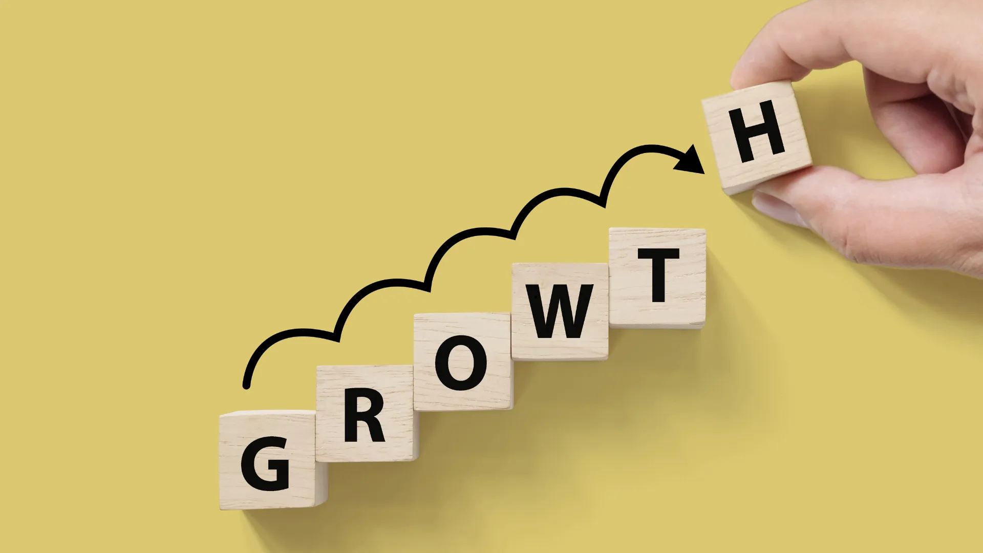 A hand placing a block with the letter "H" to complete the word "GROWTH" using wooden blocks.