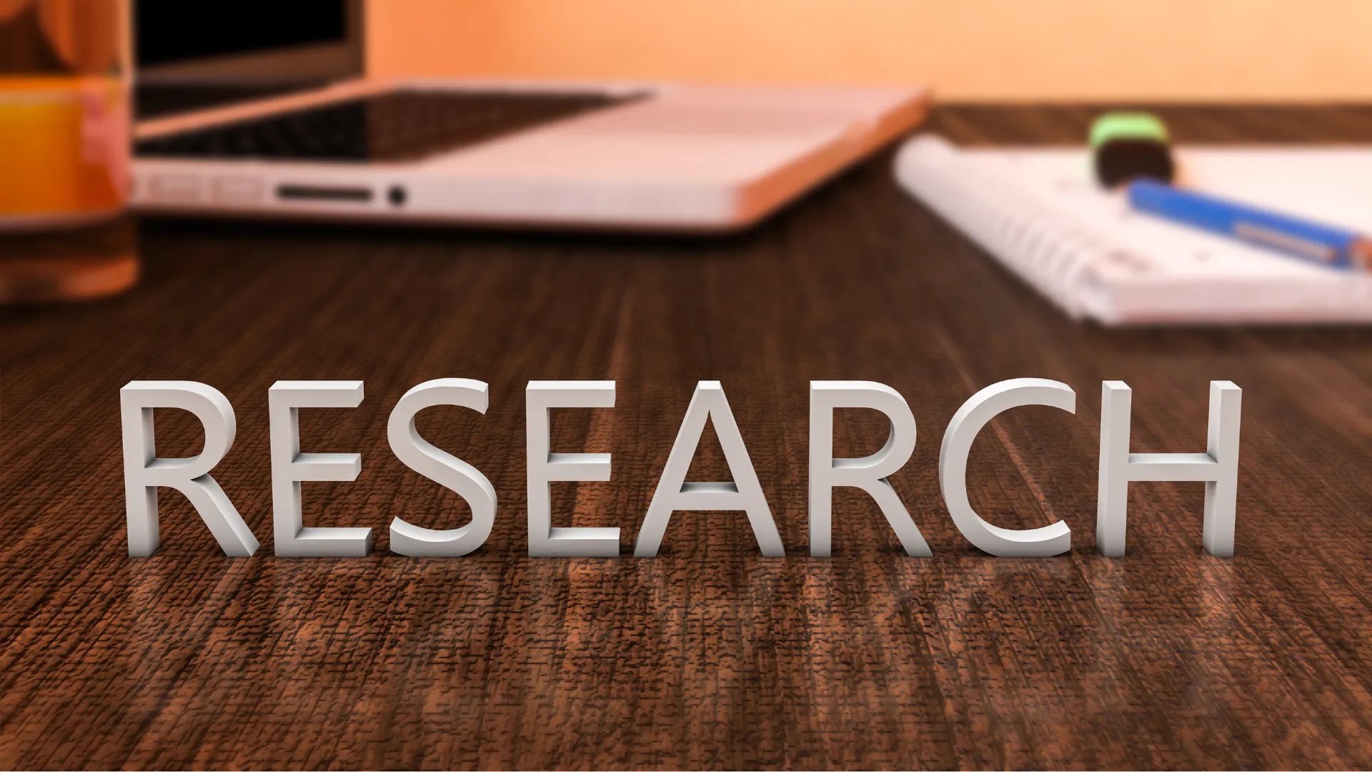 3D letters spelling 'RESEARCH' on a wooden surface with a laptop, notebook, and pen in the background