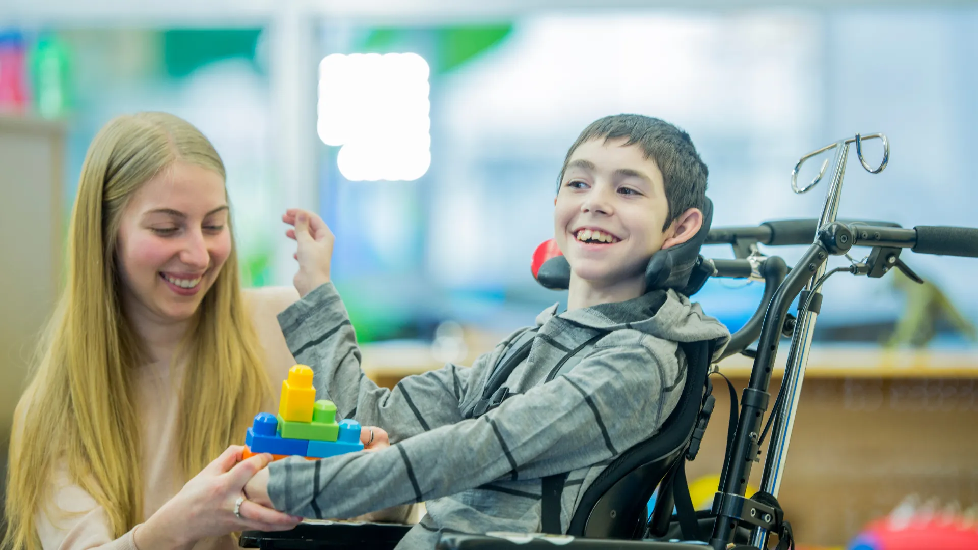 A child in a wheelchair being assisted with colourful building blocks by an adult