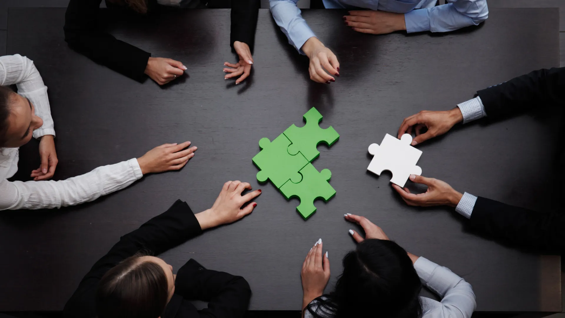A group of people sitting around a table, assembling green and white puzzle pieces.