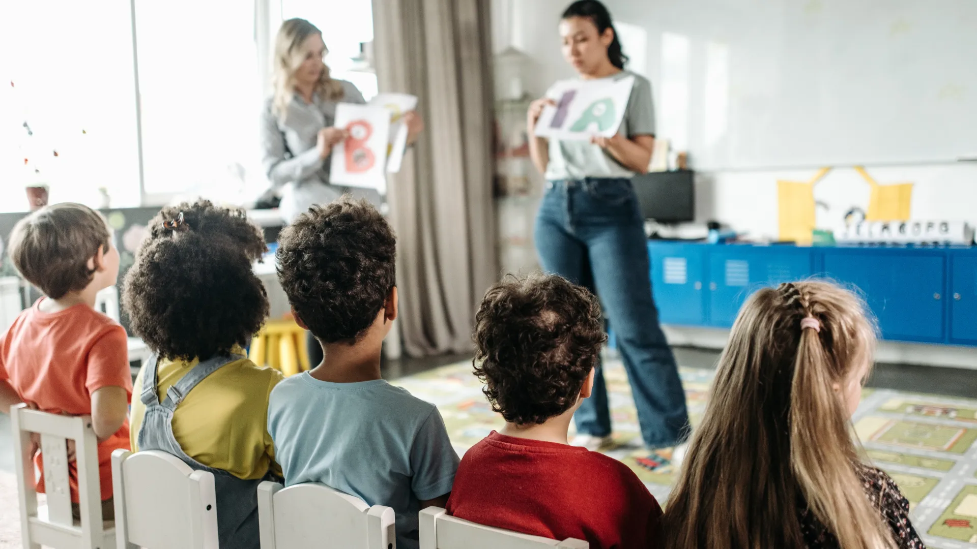 Children in a classroom learning the alphabet from two adults holding up letters