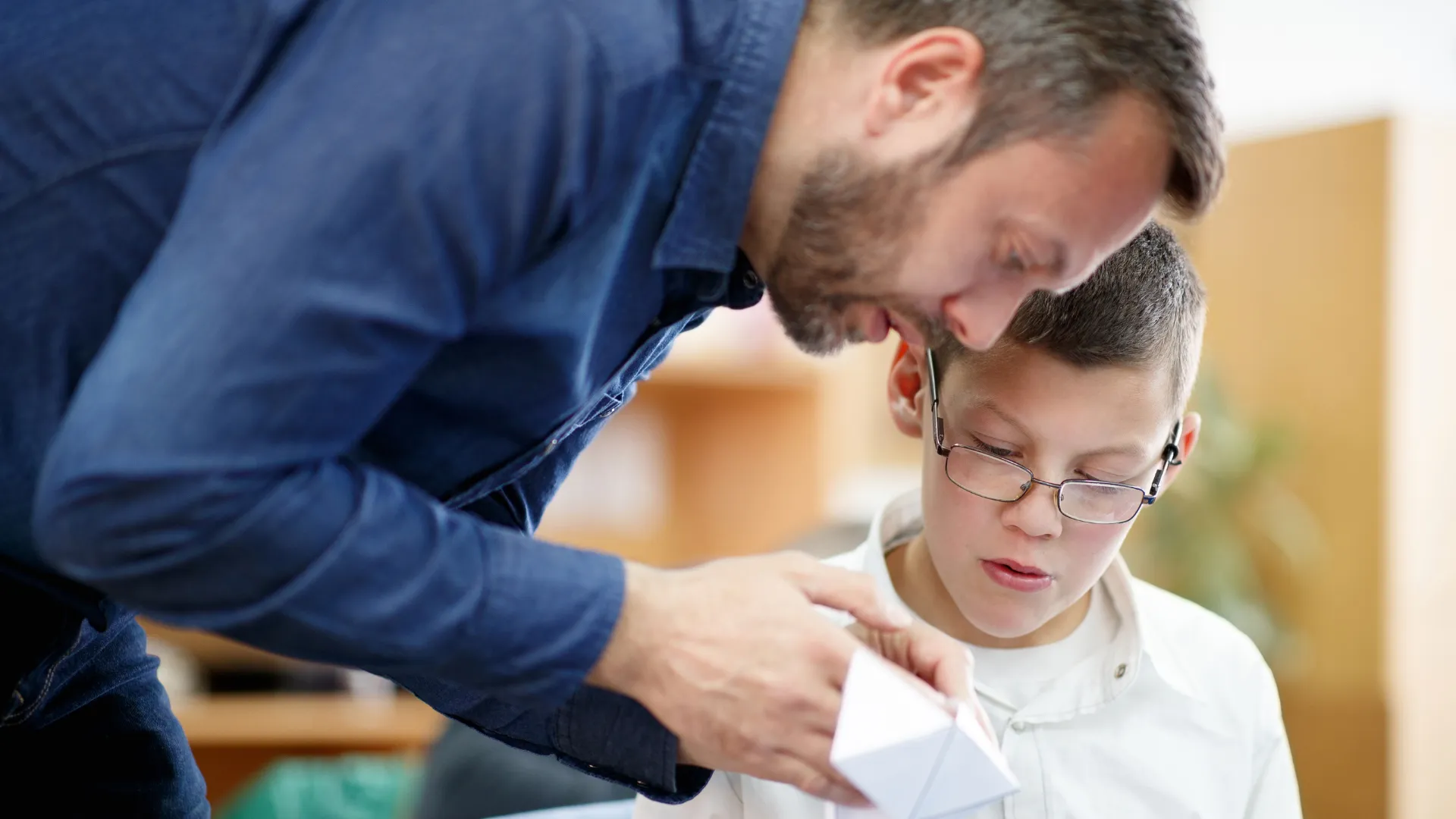 An adult assisting a child with a paper craft