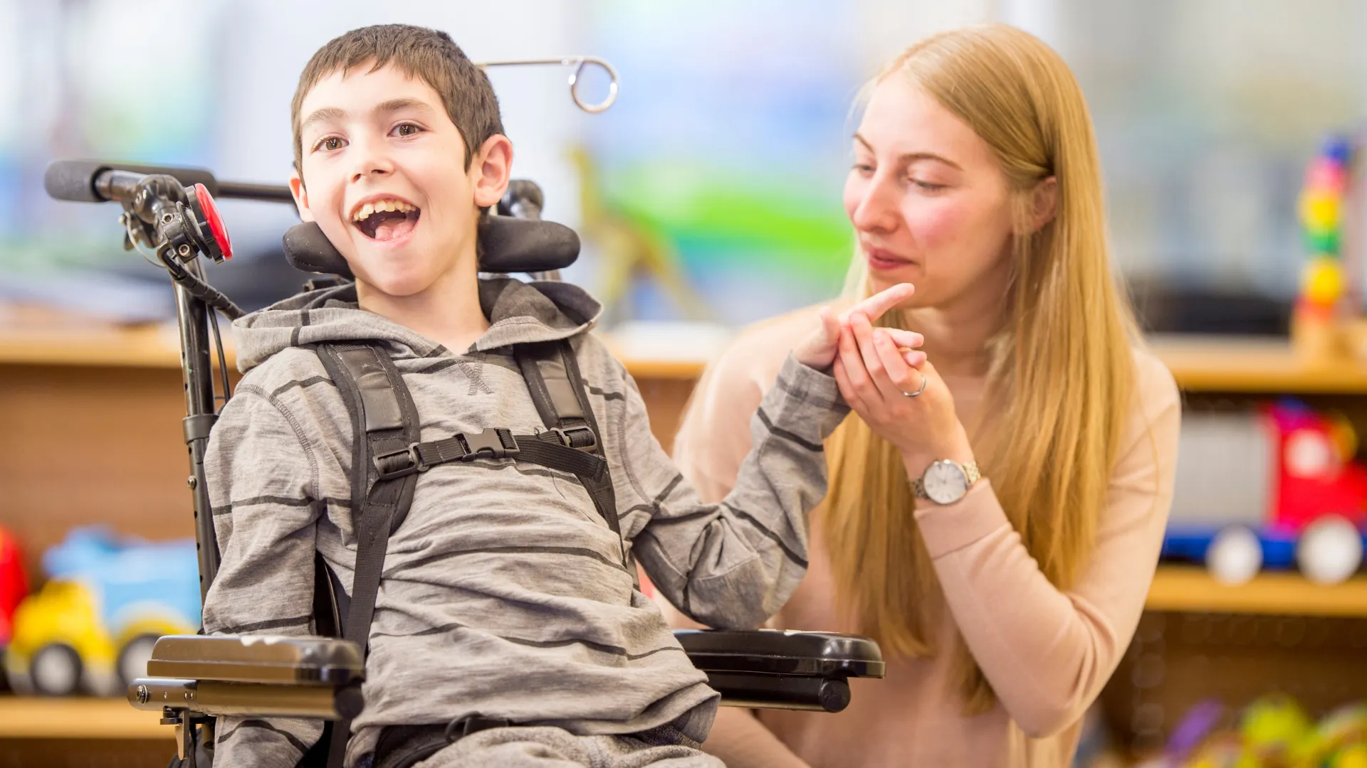 A child in a wheelchair is holding hands with an adult.