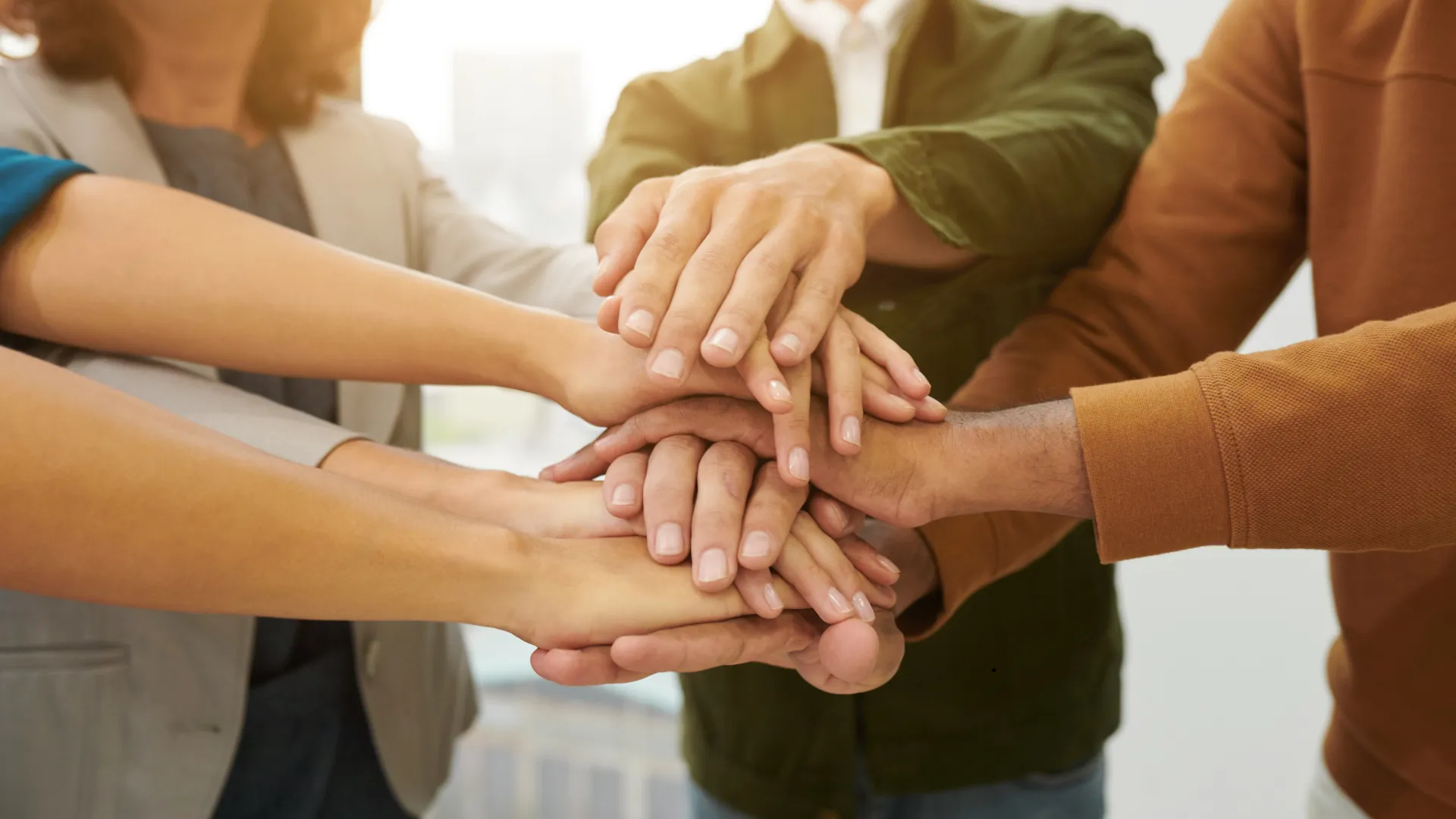 A group of people standing in a huddle placing their hands together in a gesture of teamwork