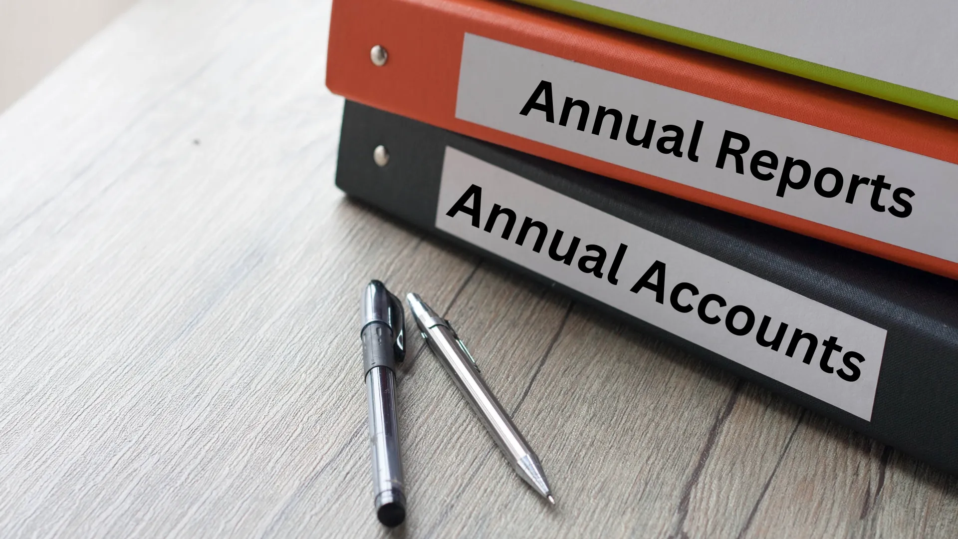 Binders labelled "Annual Reports" and "Annual Accounts" with two pens on a wooden surface.