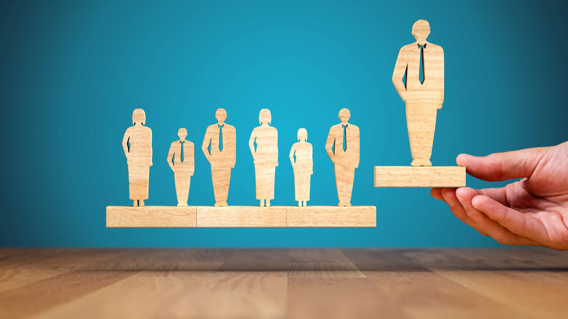 Wooden figures of business people, with one figure being elevated by a hand.
