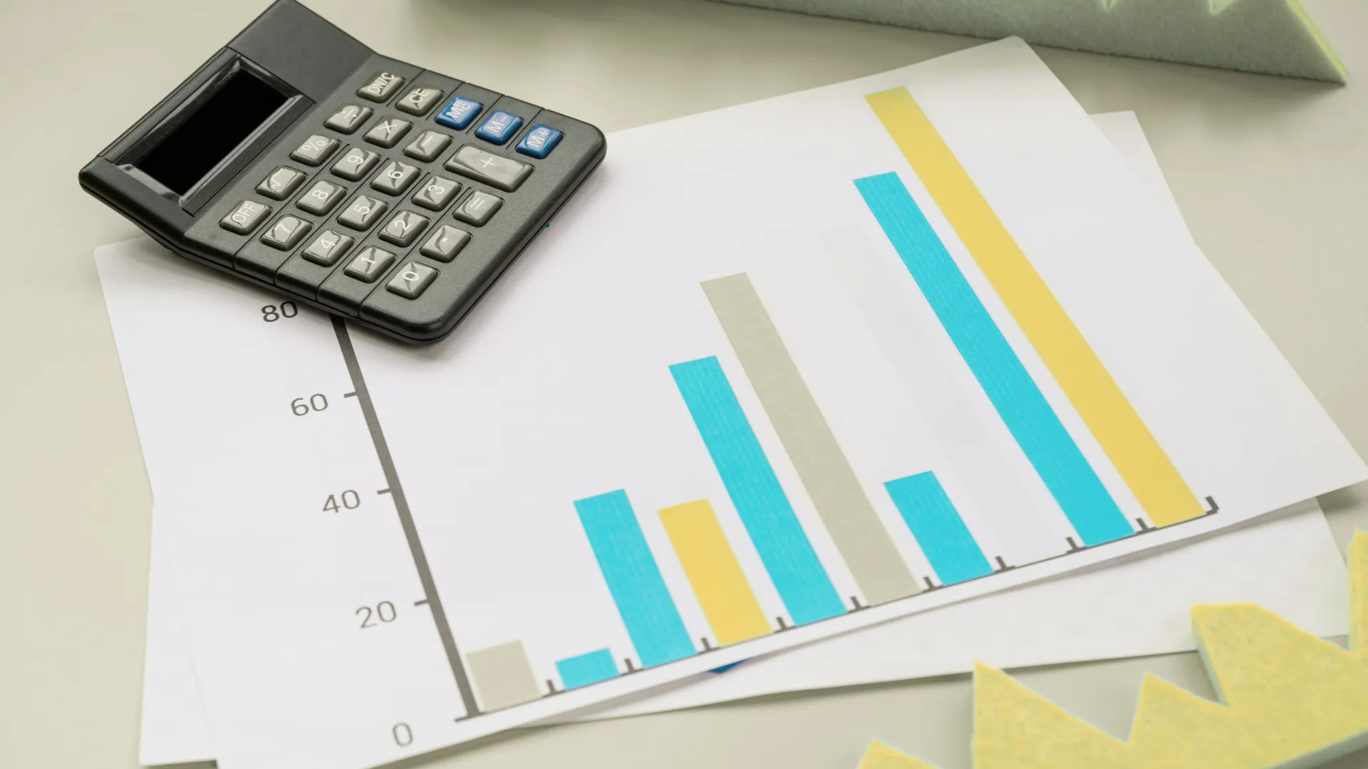 A calculator placed on top of a bar chart with blue, yellow, and grey bars.