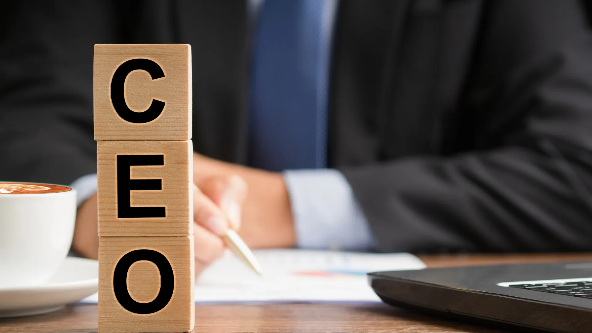 Wooden blocks spelling CEO in front of a suited person at a desk