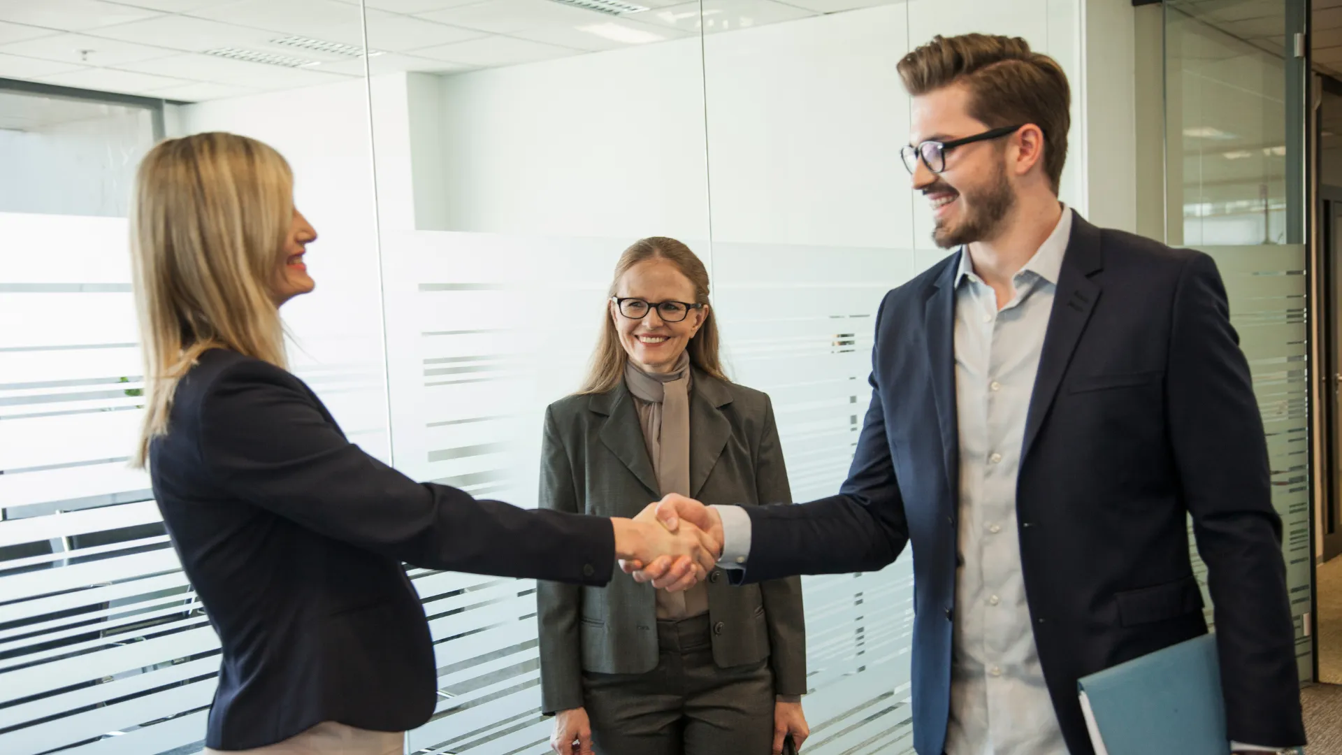 Two people shaking hands in an office while a third person stands nearby