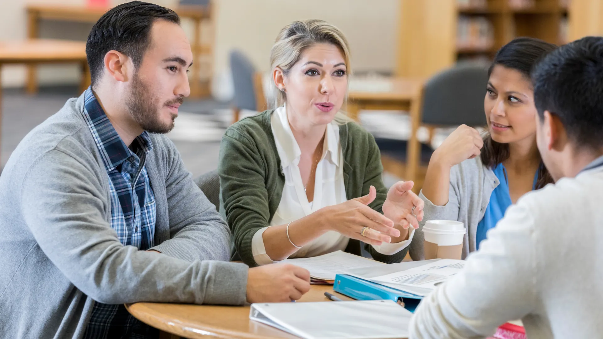 Group of people sitting at a table having a discussion with books and papers