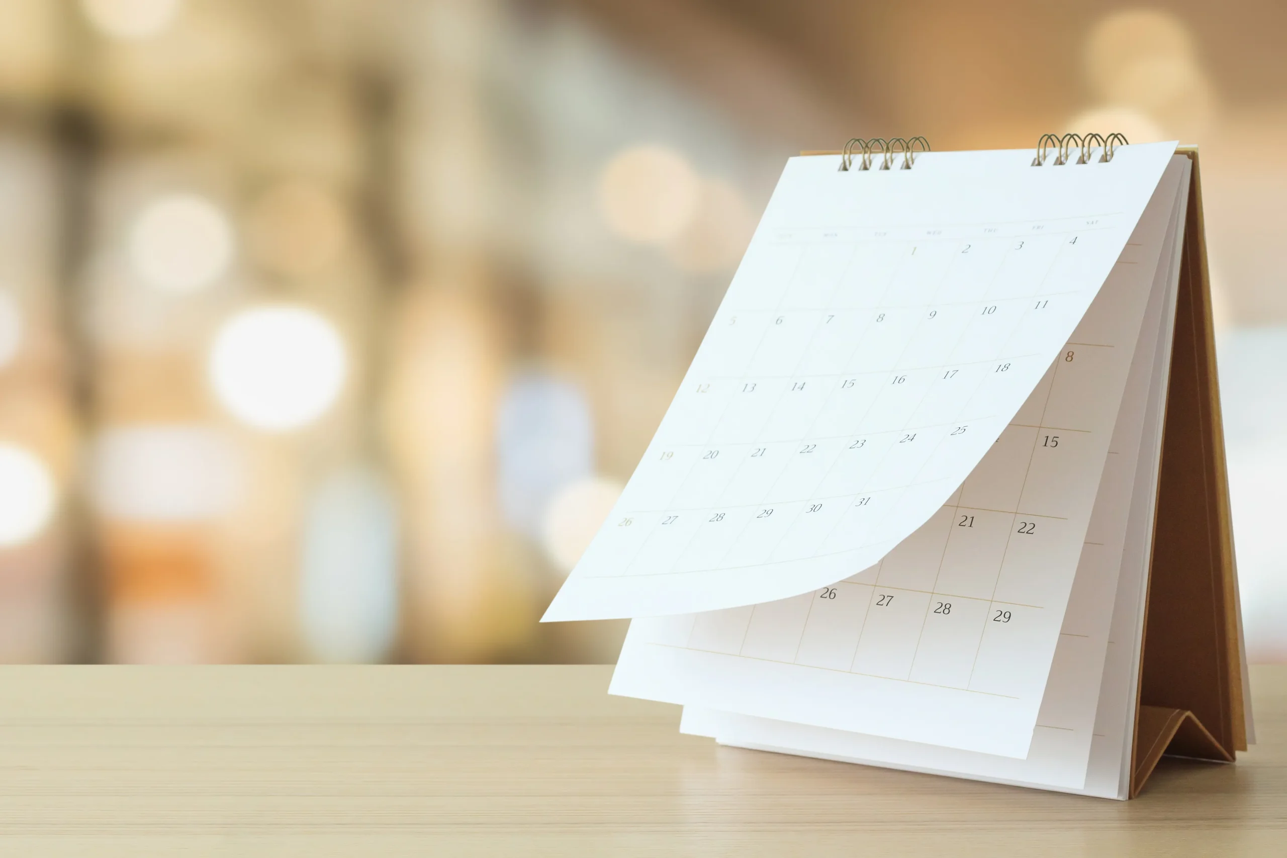A standing desk calendar with white pages placed on a light wooden surface