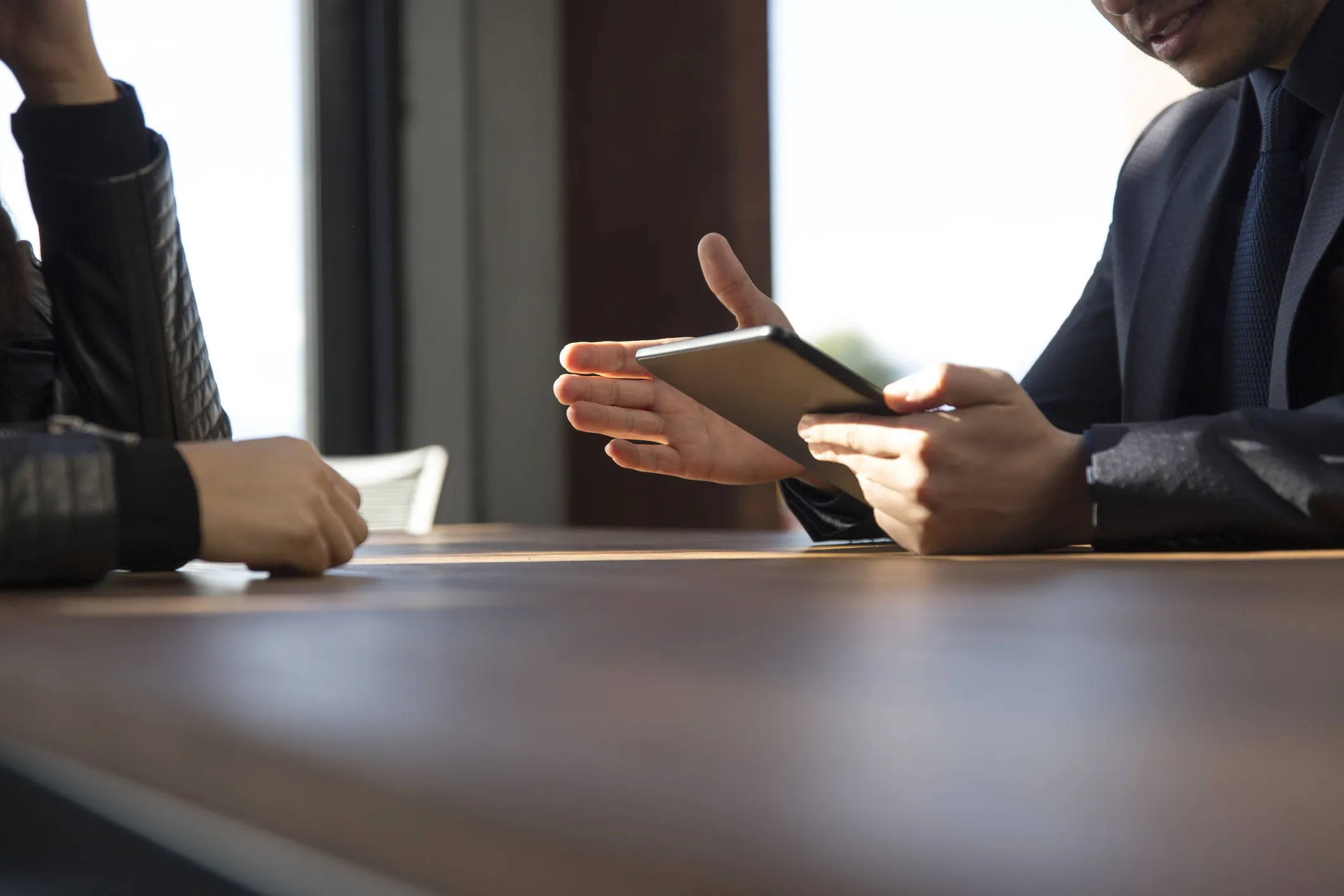 Two people sitting at a table, one holding a tablet having a discussion.