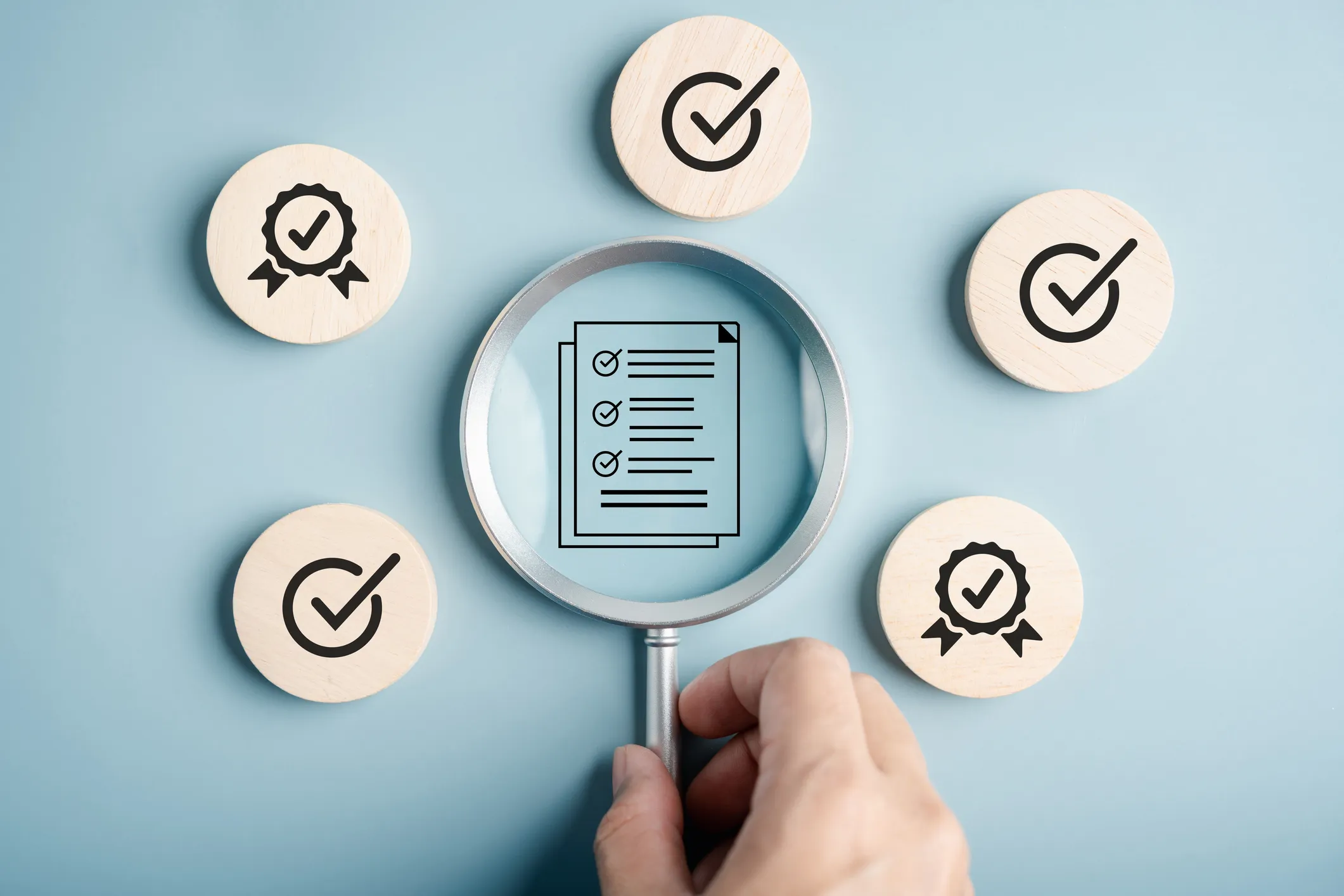 Magnifying glass focusing on a checklist icon surrounded by check mark and award symbols.