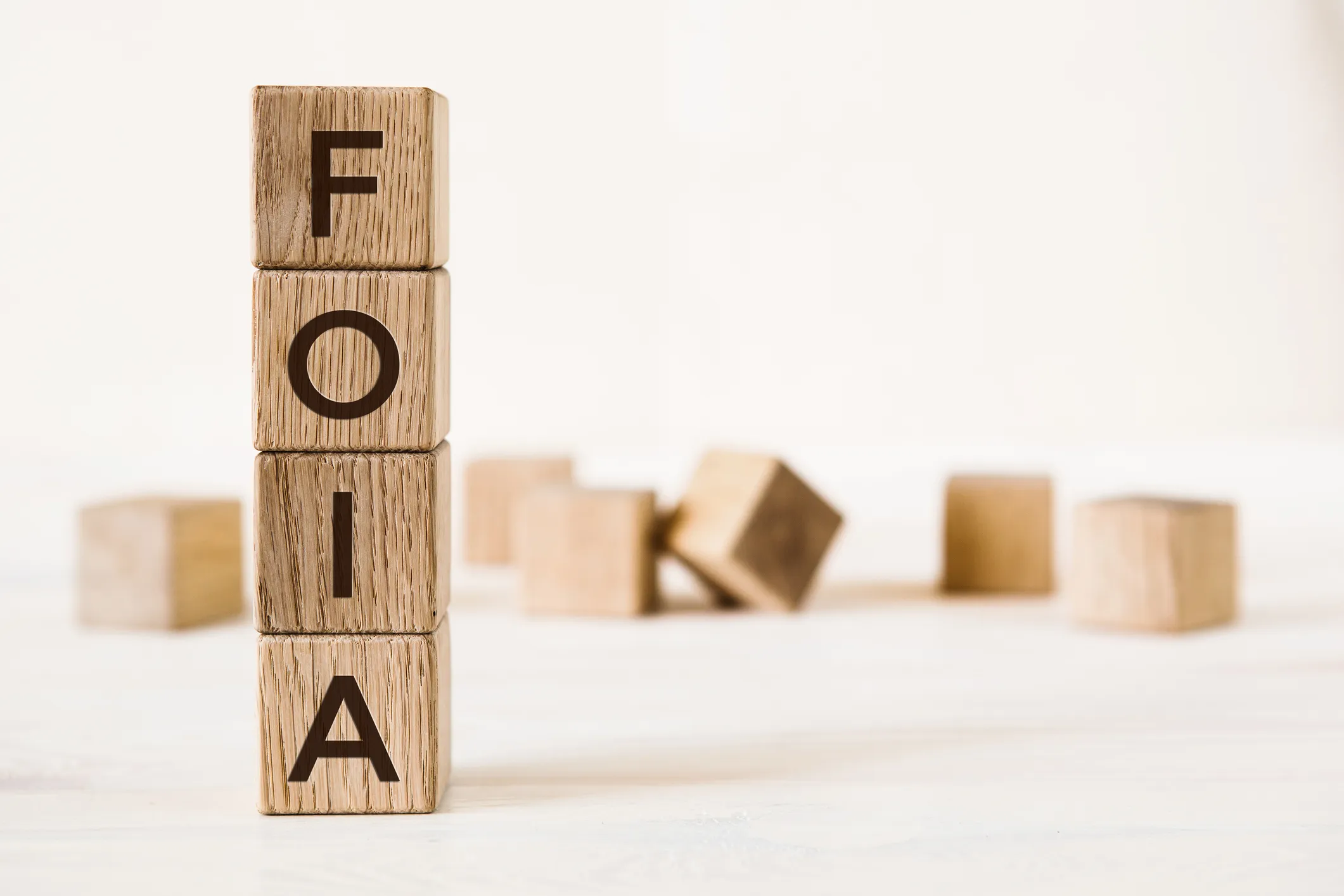 A vertical stack of four wooden blocks with letters spelling “FOIA,” an acronym for Freedom of Information Act with other blurred wooden blocks scattered in the background.
