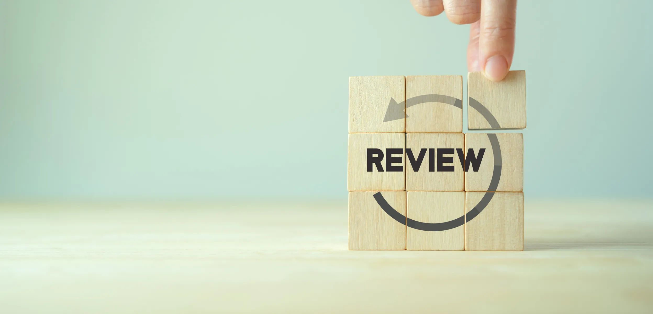 Hand placing final wooden block in puzzle with the word "REVIEW" and circular arrow