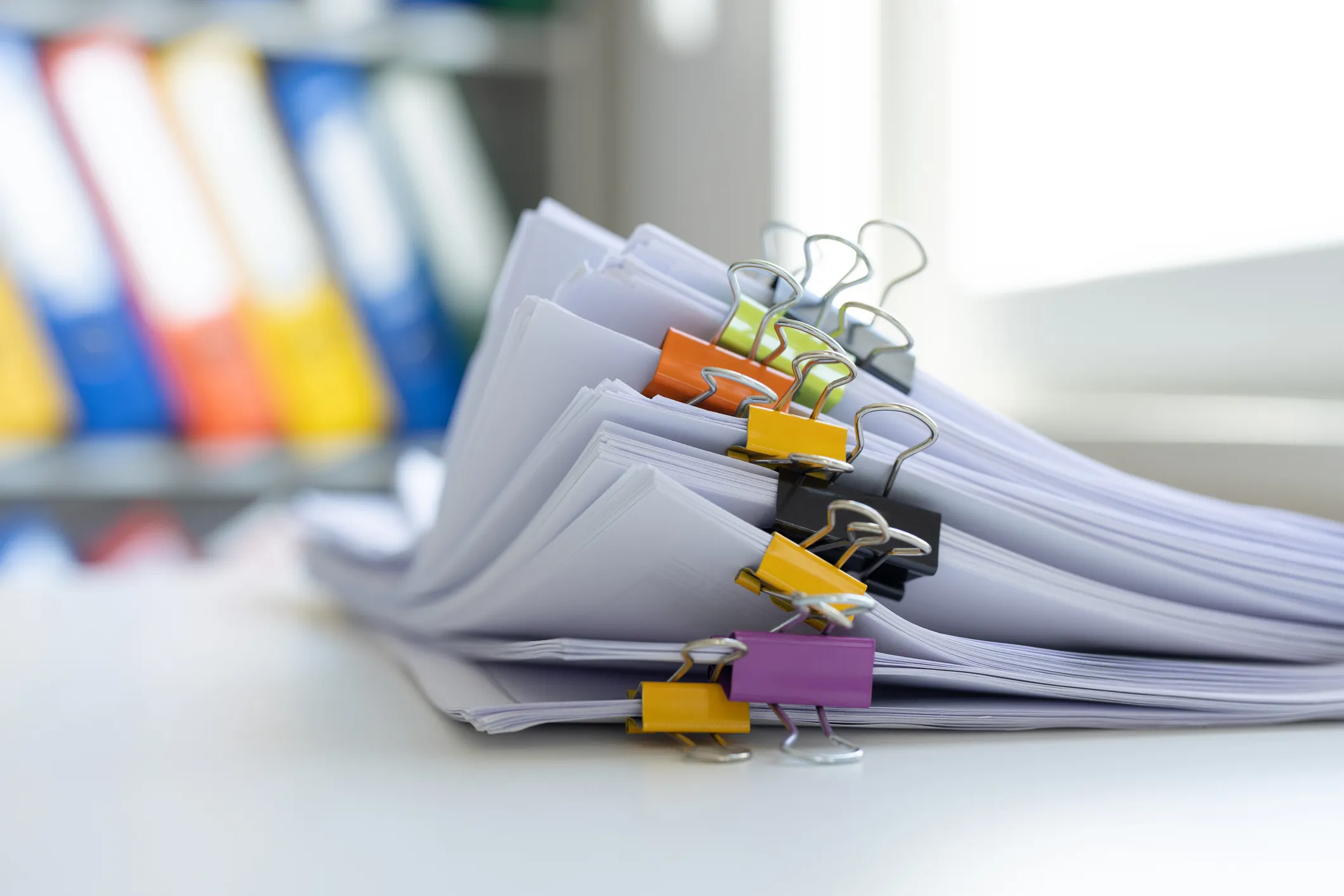 A stack of documents secured with colorful binder clips, placed on a white desk