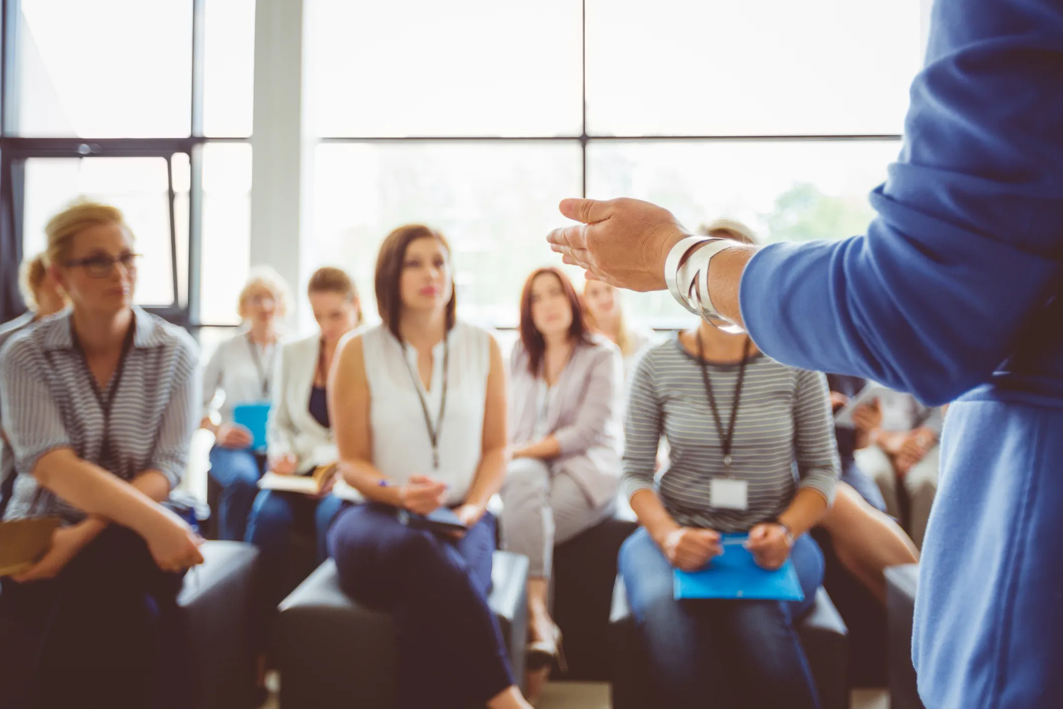 A group of people seated listening to a person standing in front of them suggesting a presentation or discussion setting.